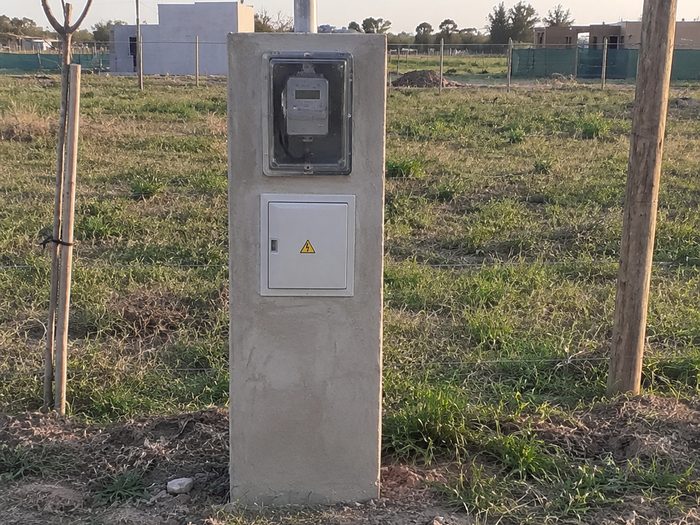 Pilar de luz terminado sobre la línea municipal, con el medidor y el tablero de conexión montados, visto desde la vereda.